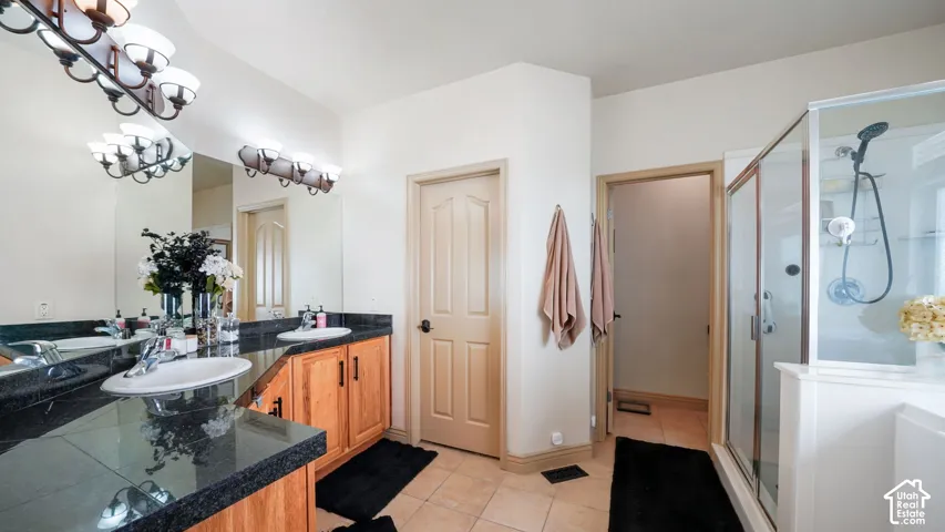Dual vanity with dark stone countertops, wood-finish cabinetry, and ceramic tile flooring