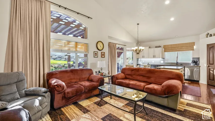 Vaulted ceiling with a chandelier, large arched window, wood-finish flooring, white cabinetry, and stainless steel appliances