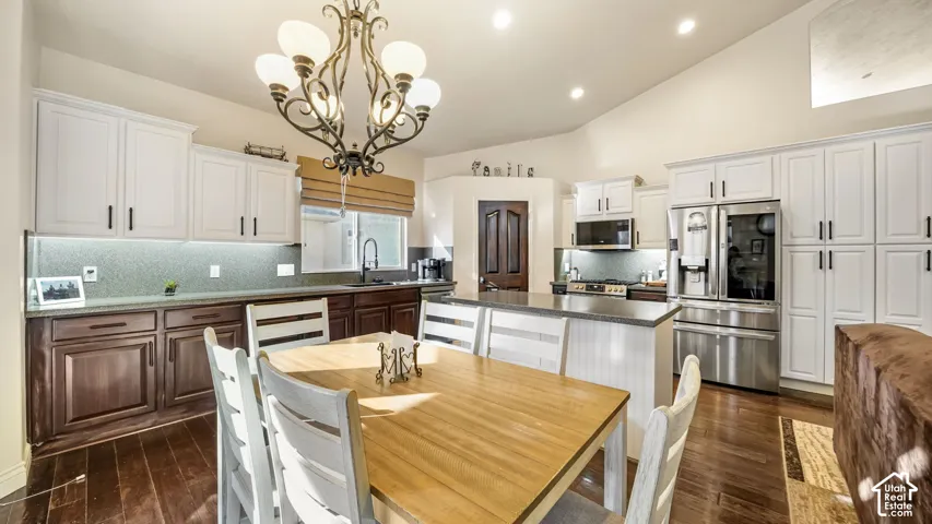 Vaulted ceiling kitchen featuring two-tone cabinetry, stainless steel appliances, and a central island with a luxury countertop