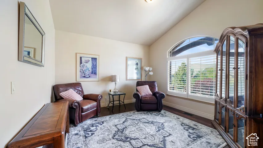 Piano Room with and Vaulted ceiling with an arched window, plantation shutters, and wood looring