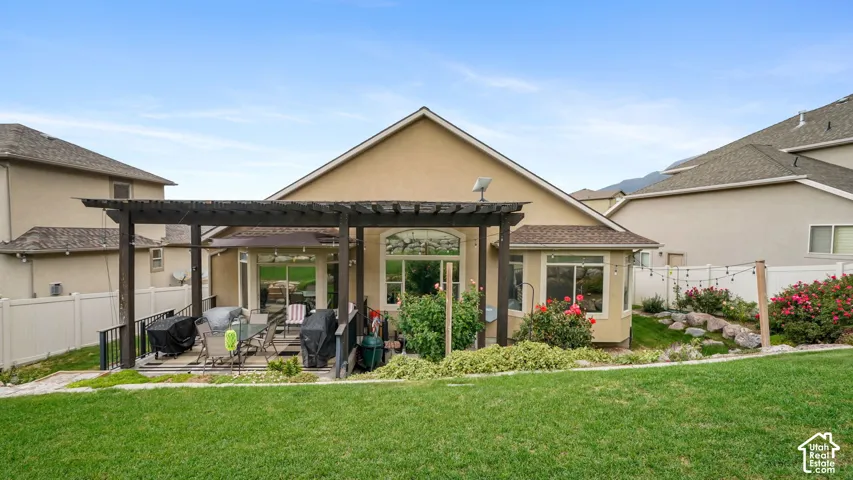 Expansive backyard featuring a manicured lawn, a wooden pergola-covered patio, and a rock garden with rose bushes