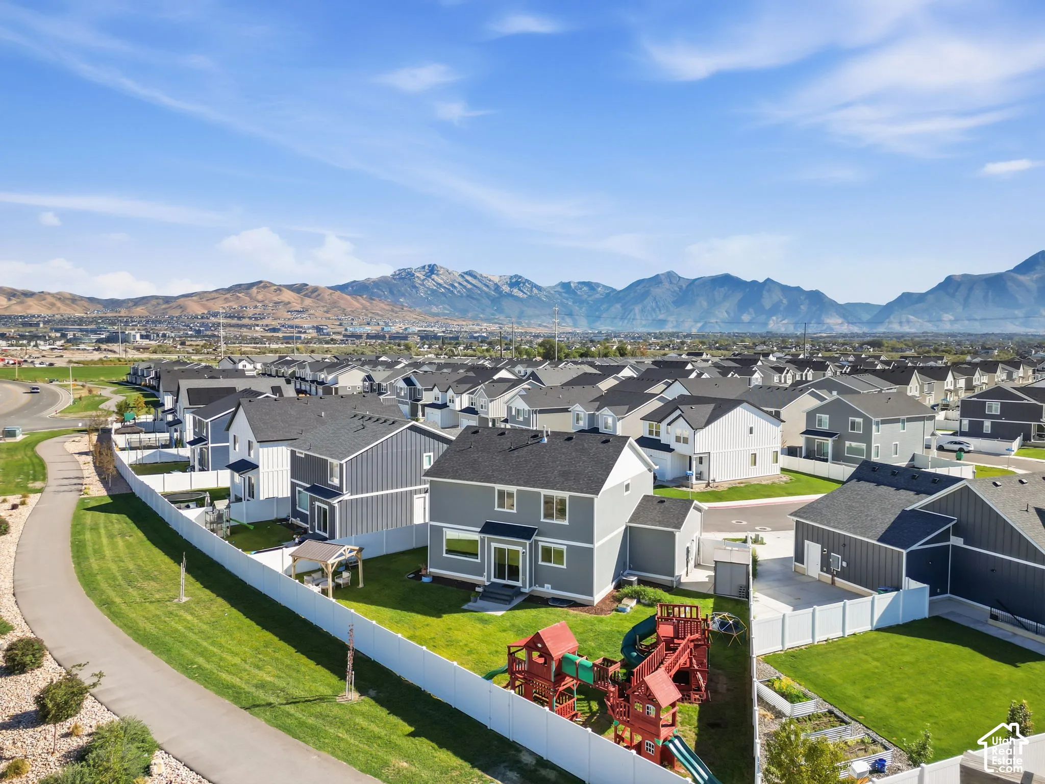 Expansive backyard featuring a manicured lawn, white privacy fencing, and mountain scenery
