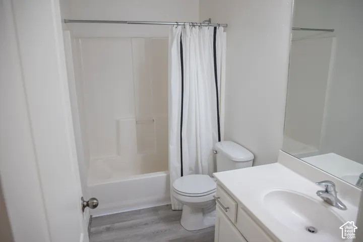 White bathtub with an integrated shower, light wood-finish flooring, and a vanity with a white countertop