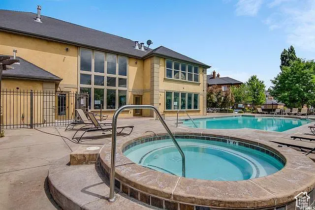 Outdoor swimming pool with integrated hot tub, surrounded by a concrete patio