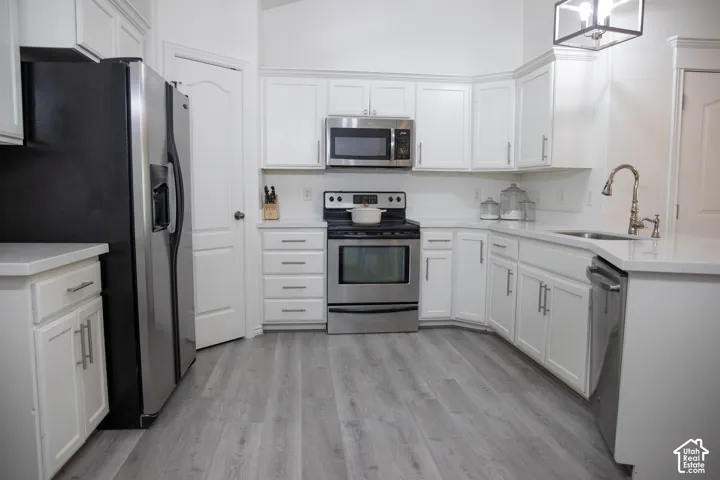 White cabinetry, stainless steel appliances, light-toned wood-finish flooring, white countertops, and a subway tile backsplash