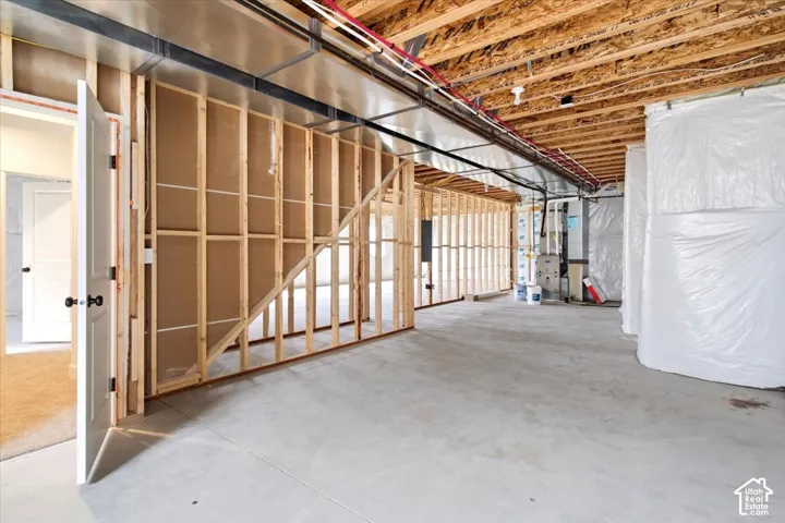 Unfinished basement with concrete flooring, exposed wood framing, and accessible utilities