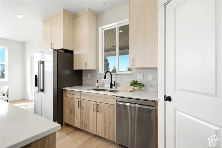 Contemporary kitchen featuring light wood-finish cabinetry, stainless steel appliances, a single basin sink with a black gooseneck faucet, white subway tile backsplash, and light-toned countertops