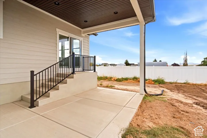 Expansive concrete patio with covered awning, leading to exterior stairs with wrought iron railing