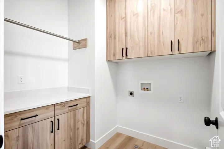 Wood-finish flooring with white baseboards, a wall-mounted drying rod, white countertop, and wood-finish cabinetry featuring black hardware