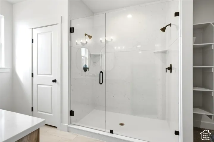 Glass-enclosed shower with a bronze-finish showerhead and controls, integrated shower niche, and white shower pan