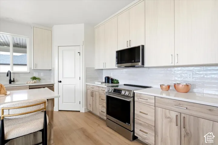 Modern kitchen featuring light wood-finish cabinetry, white countertops, stainless steel appliances, a subway tile backsplash, and light wood-finish flooring