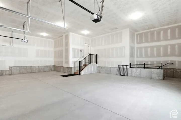 Spacious garage featuring a concrete floor, built-in stairs with black metal railings, and integrated overhead lighting