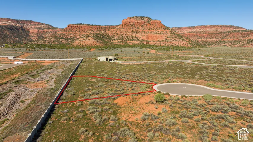 Expansive desert lot featuring natural vegetation, a concrete wall boundary, and a paved cul-de-sac