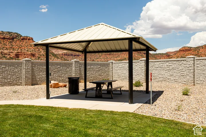 Permanent metal gazebo with a picnic table, concrete paver flooring, and a decorative stone-look privacy wall