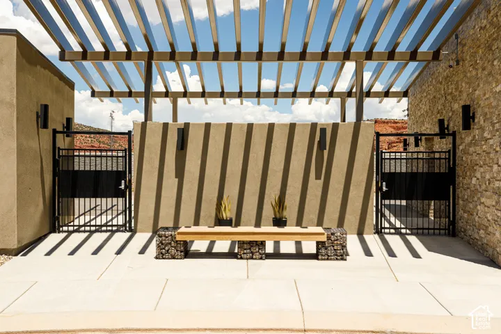 Pergola-covered patio featuring concrete pavers, gabion bench, and wrought iron gates