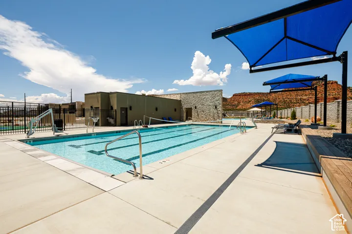 Outdoor swimming pool with concrete decking, blue shade structures, and adjacent building with stone veneer