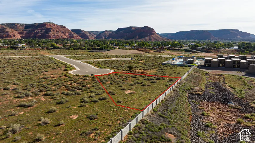 Cleared building lot with paved road access, surrounded by natural desert landscaping, and perimeter fencing