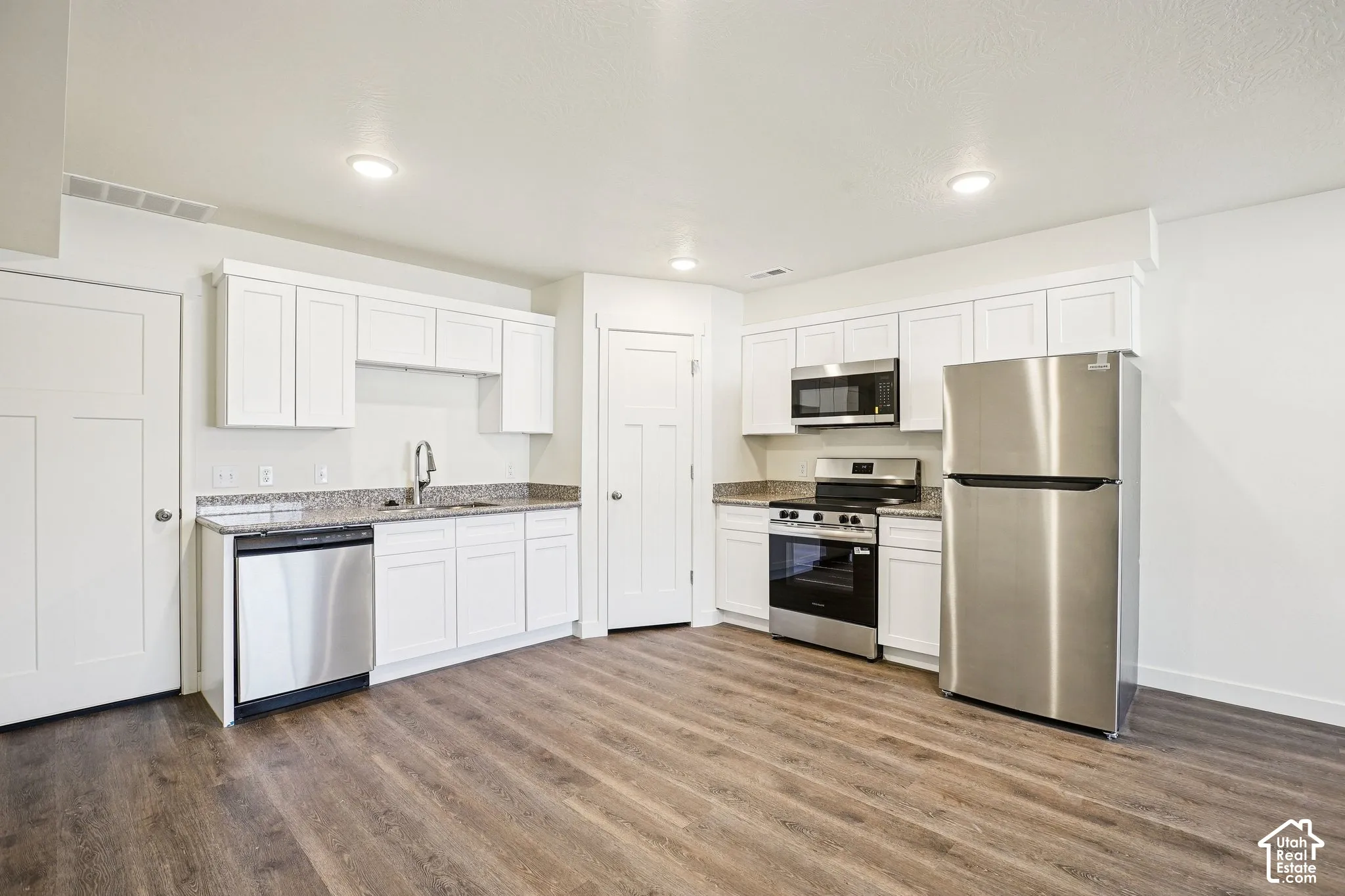 Kitchen with wood-finish flooring, white cabinetry, granite-style countertops, and stainless steel appliances