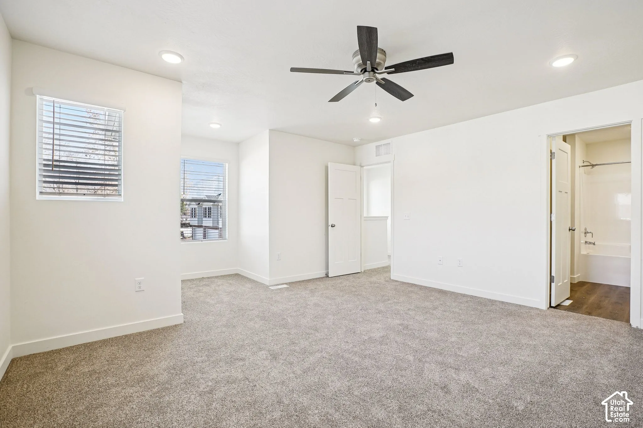 Expansive room featuring plush carpeting, multiple windows with blinds, a ceiling fan with integrated lighting, and recessed ceiling lights