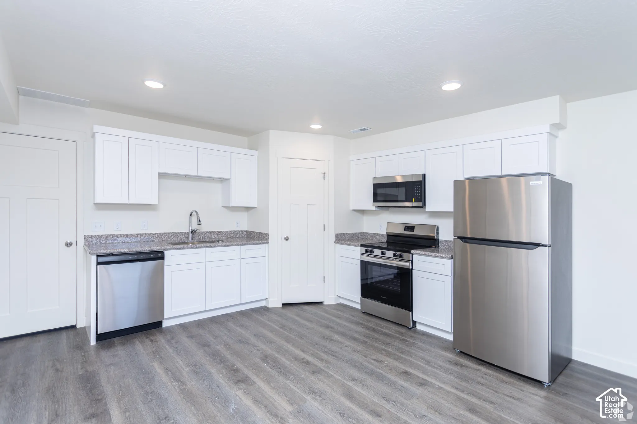 Kitchen featuring white cabinetry, granite-style countertops, stainless steel appliances, and wood-finish flooring