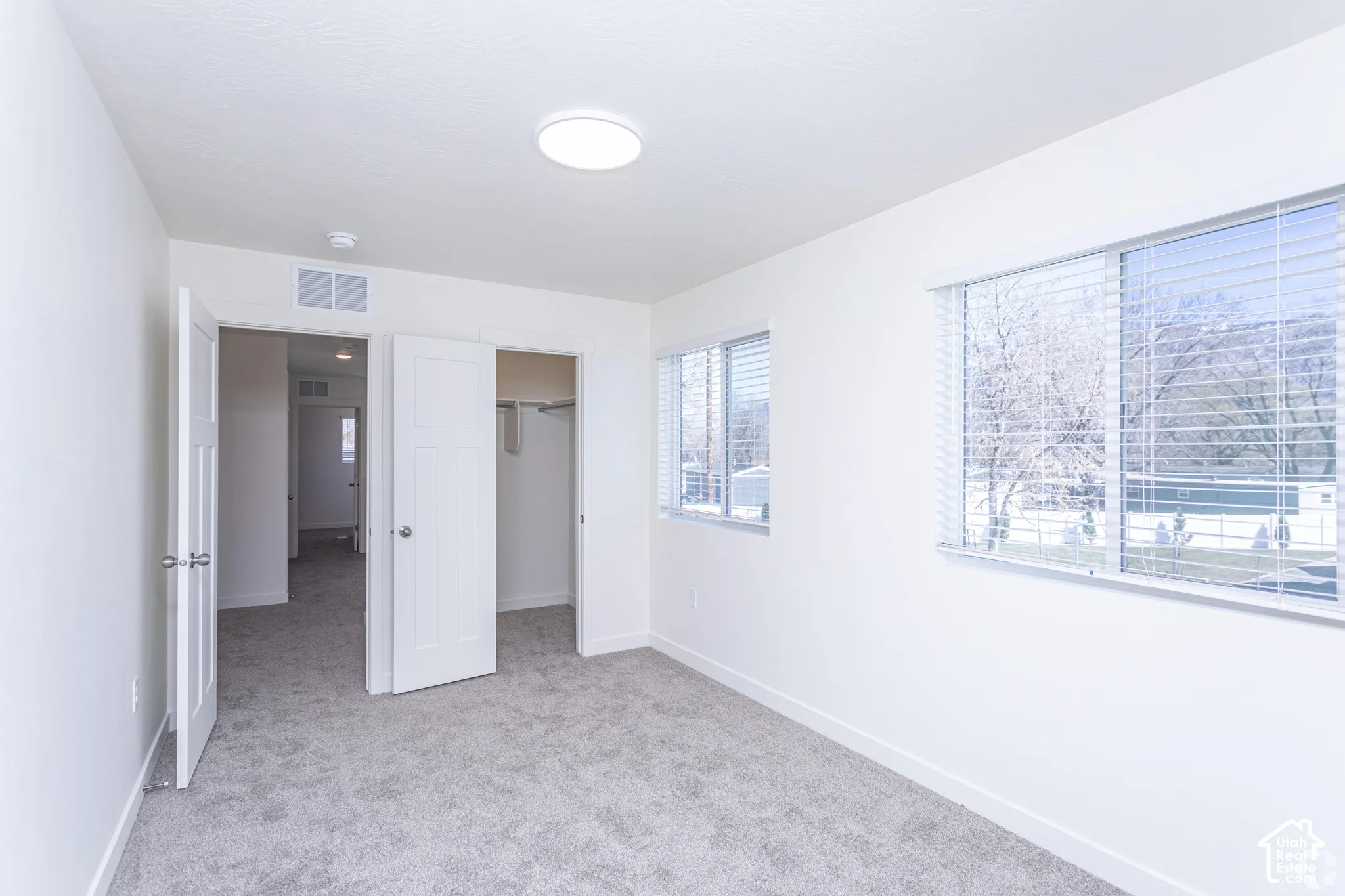 Plush grey carpeting, white interior doors, windows with blinds, built-in closet, and a flush-mount ceiling light