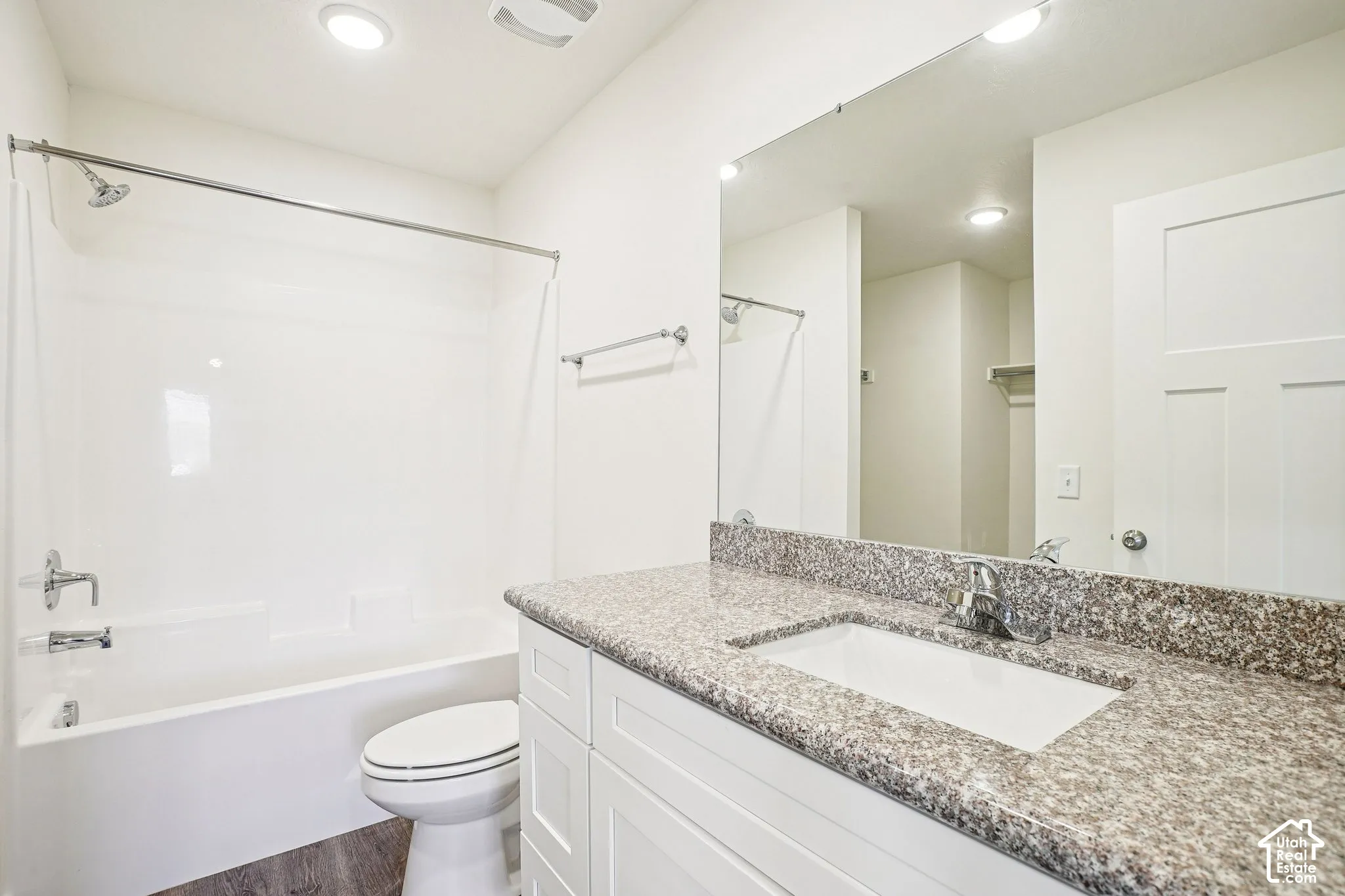White vanity with integrated sink, speckled countertop, chrome faucet, and full-width mirror