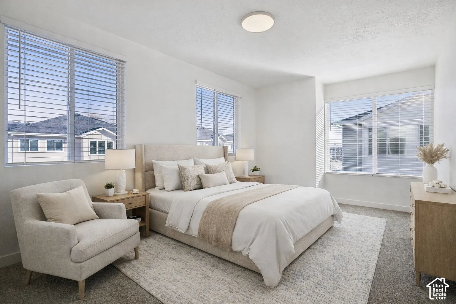 Spacious bedroom featuring multiple windows with horizontal blinds, textured carpeting, and a flush-mount ceiling light fixture