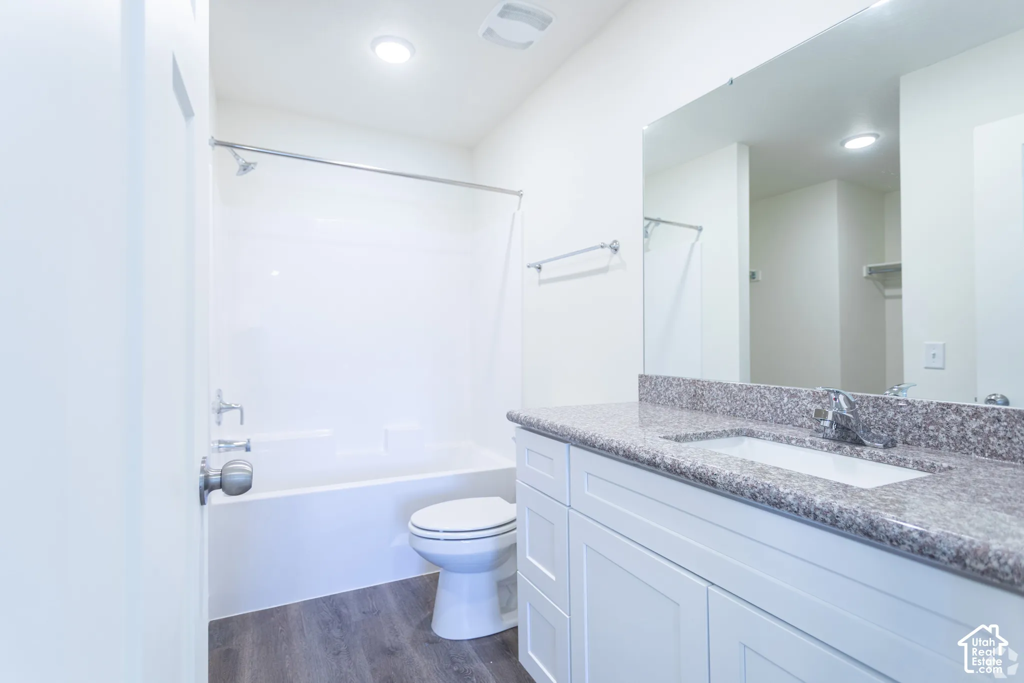 Bathroom featuring a vanity with a stone countertop, an integrated sink, a full-width mirror, a tub-shower combination, and wood-finish flooring
