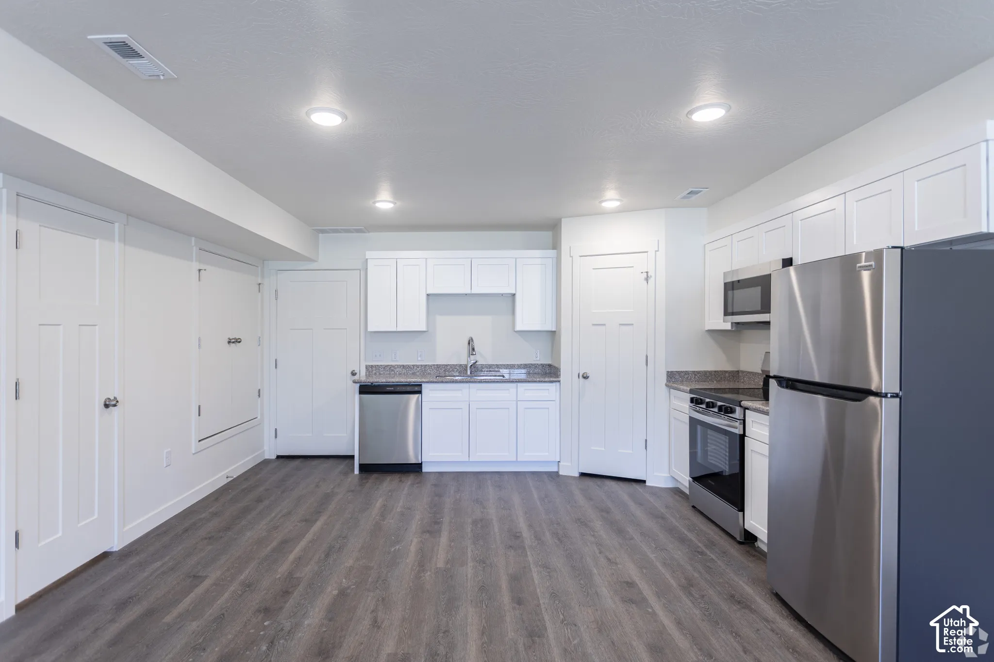 Contemporary kitchen space featuring white shaker cabinetry, stainless steel appliances, wood-finish flooring, recessed lighting, and a neutral-toned backsplash