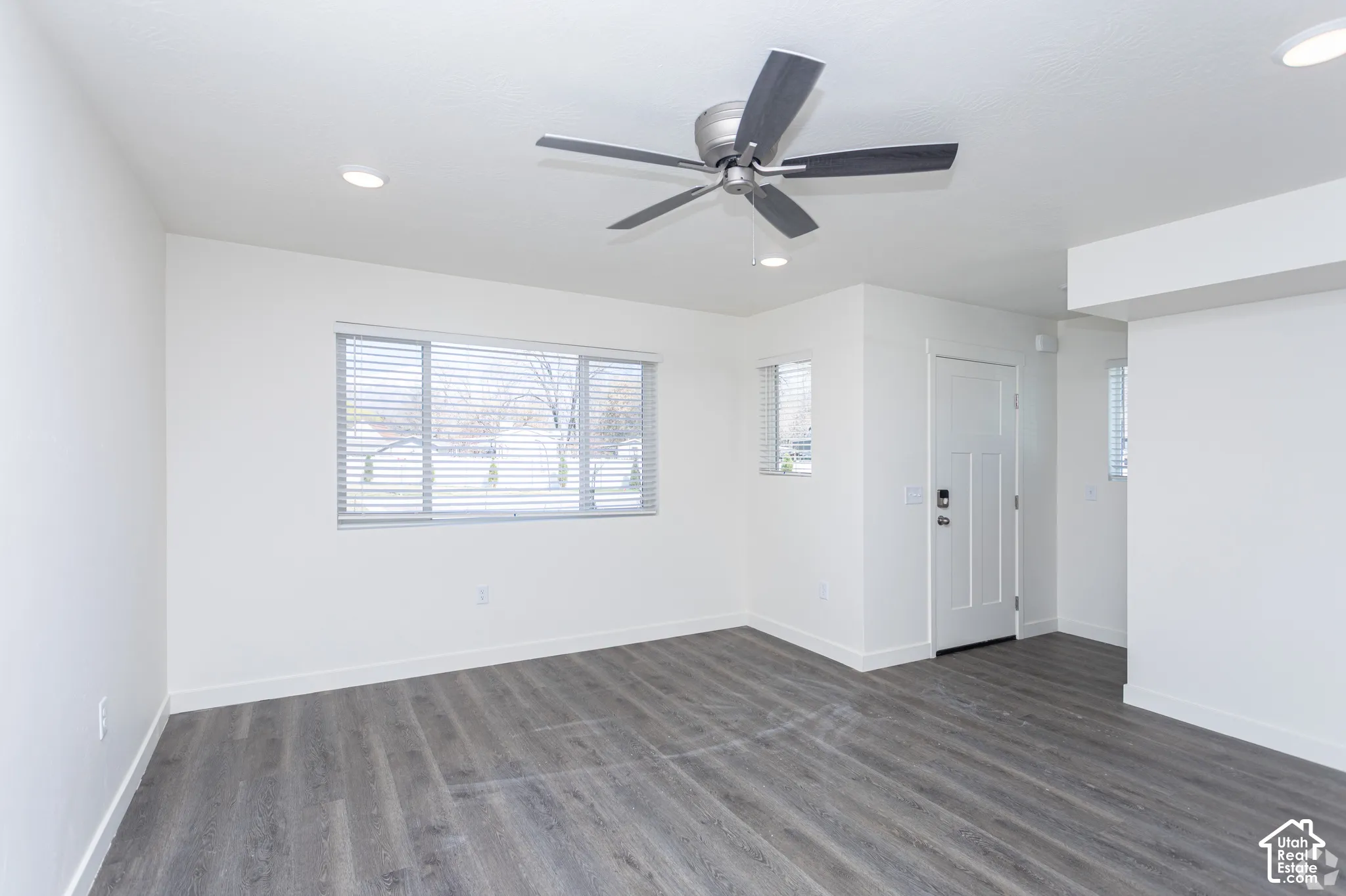 Spacious room featuring wood-finish flooring, a large window with blinds, recessed lighting, and a ceiling fan