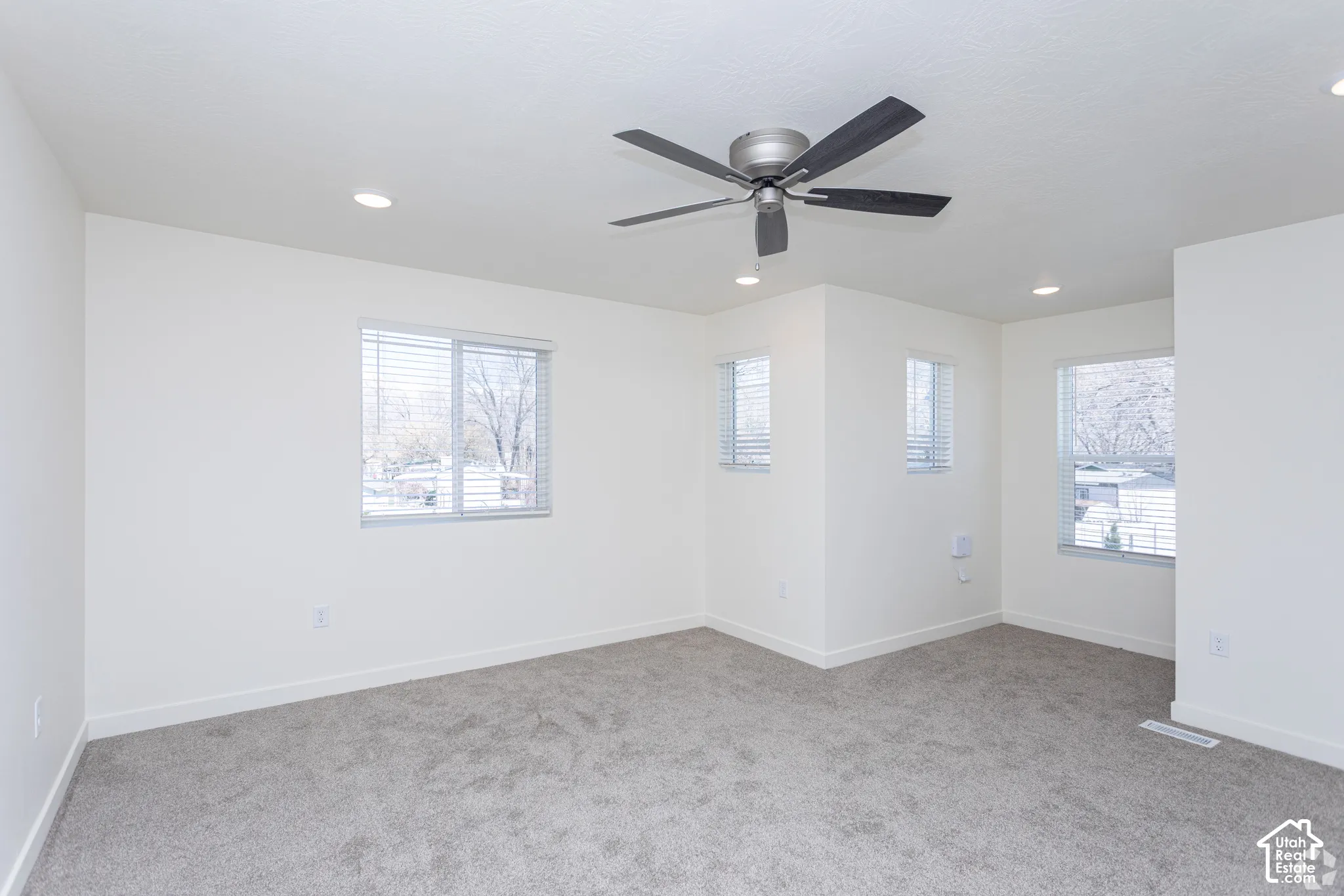 Recessed lighting, ceiling fan, multiple windows with blinds, and neutral carpeting
