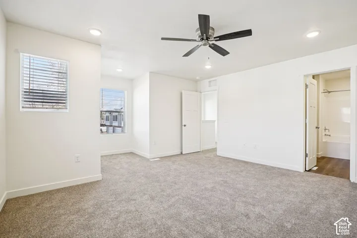 Expansive room featuring plush carpeting, multiple windows with blinds, a ceiling fan with integrated lighting, and recessed ceiling lights