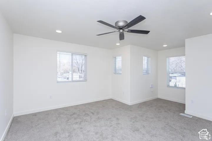 Recessed lighting, ceiling fan, multiple windows with blinds, and neutral carpeting