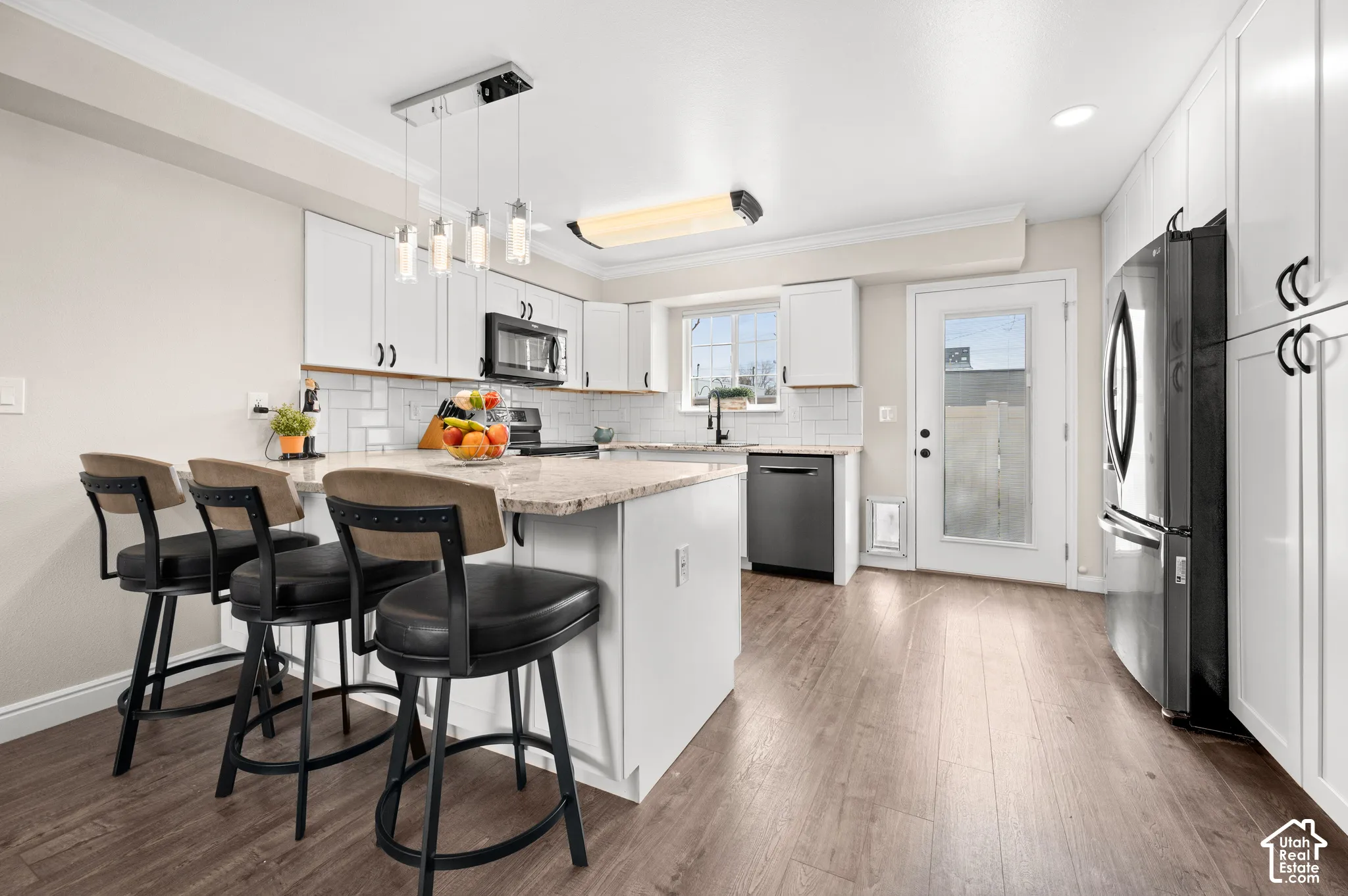Kitchen featuring wood-finish flooring, white cabinetry, a light-toned countertop, stainless steel appliances, and a subway tile backsplash