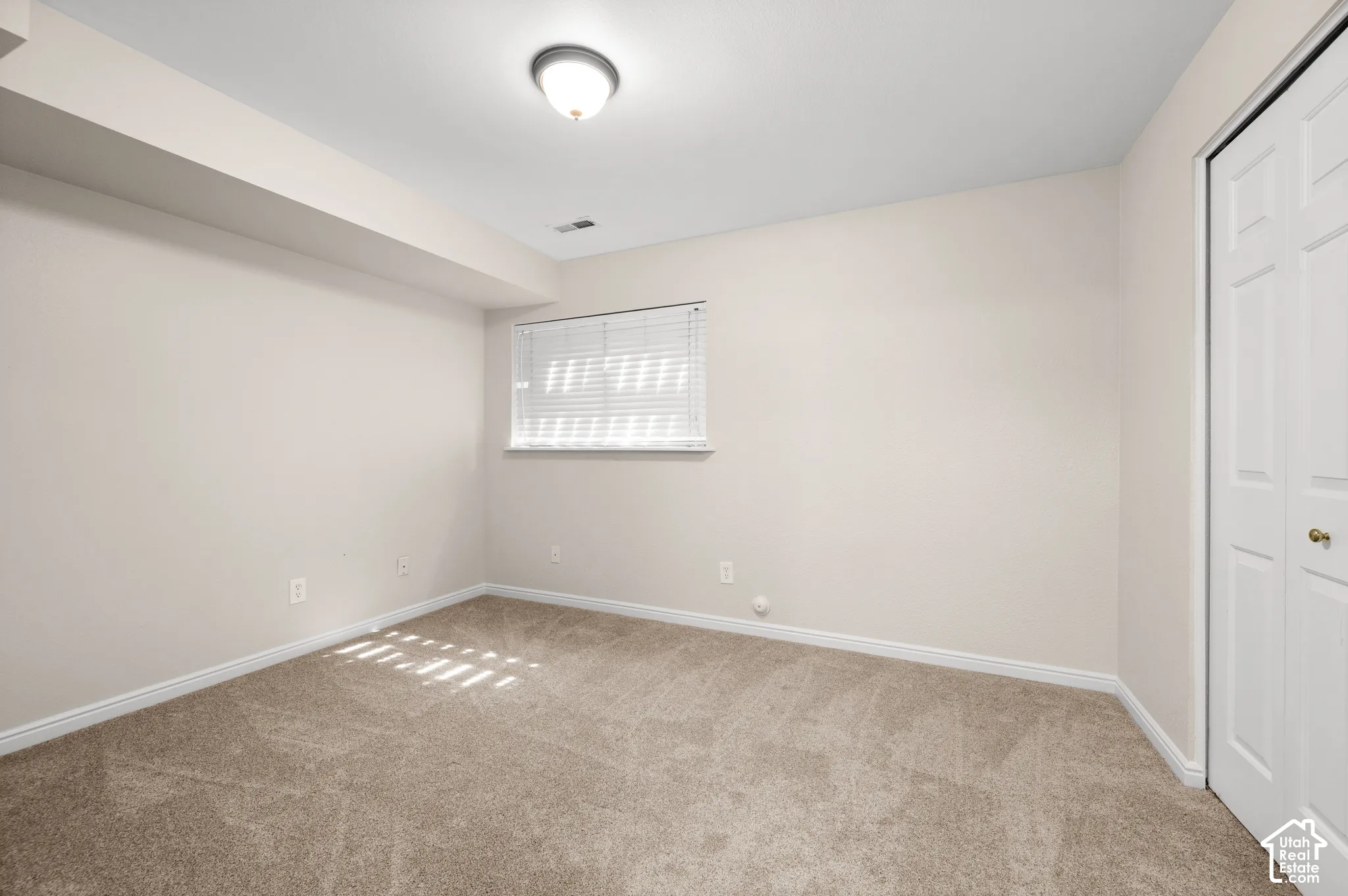 Neutral-toned carpeting, window with horizontal blinds, flush mount ceiling light, and bi-fold closet doors