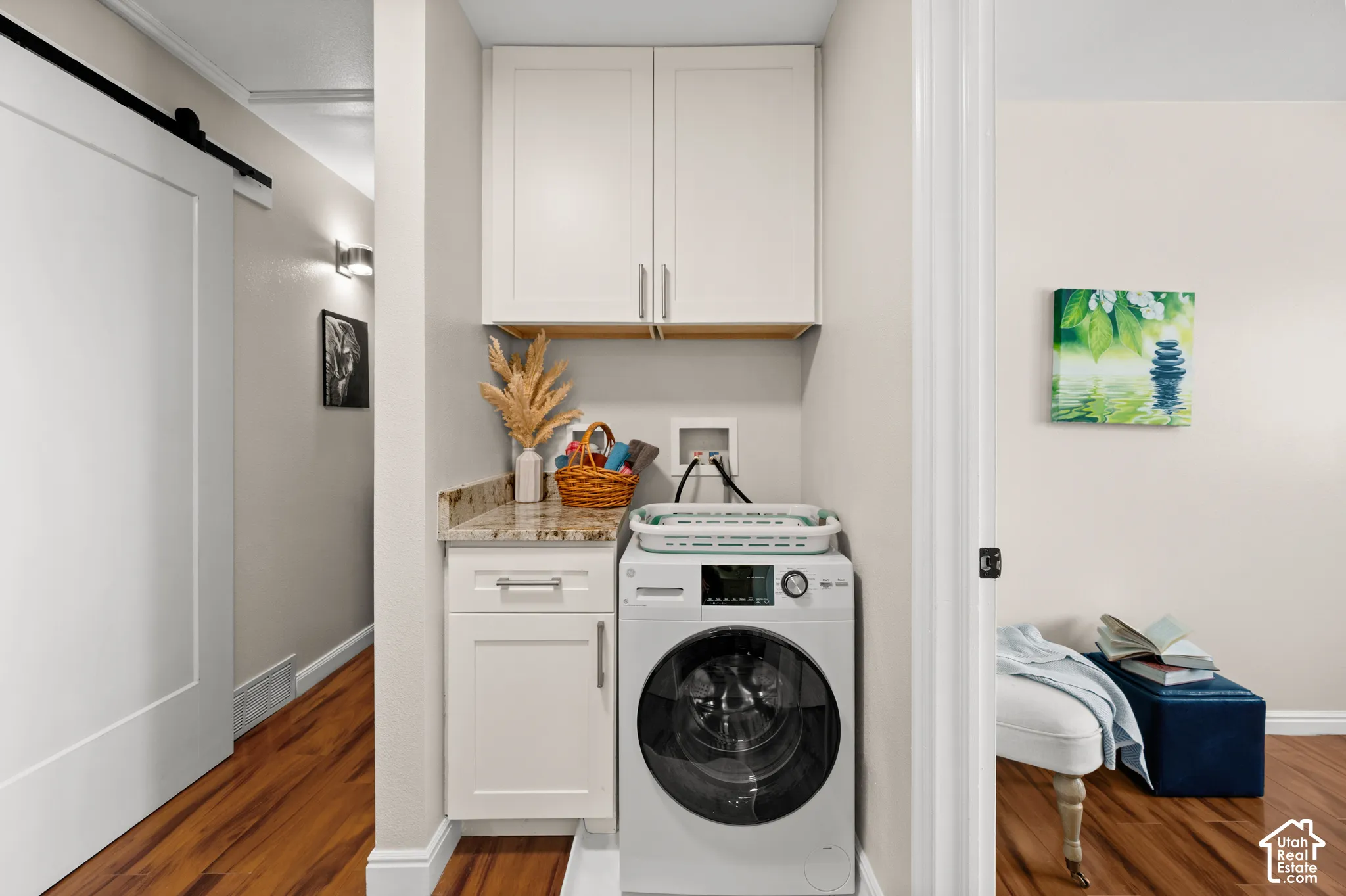 Dedicated laundry area featuring a front-load washing machine, white cabinetry, a built-in counter with a stone surface, and wood-finish flooring