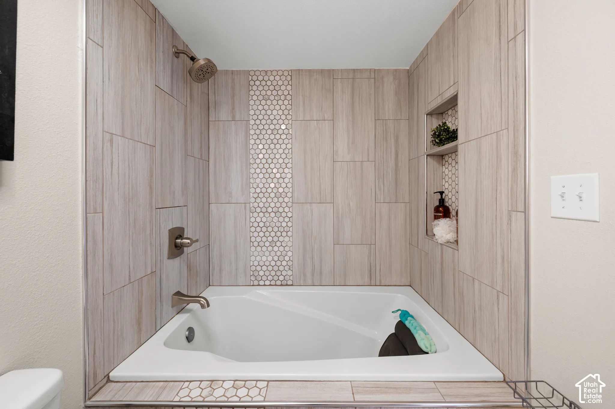Alcove bathtub featuring a tiled surround, accent mosaic tile, and built-in shower niches