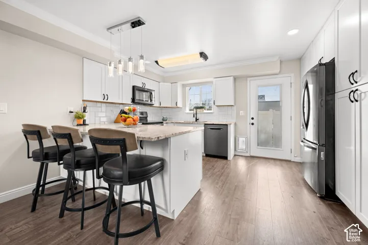 Kitchen featuring wood-finish flooring, white cabinetry, a light-toned countertop, stainless steel appliances, and a subway tile backsplash