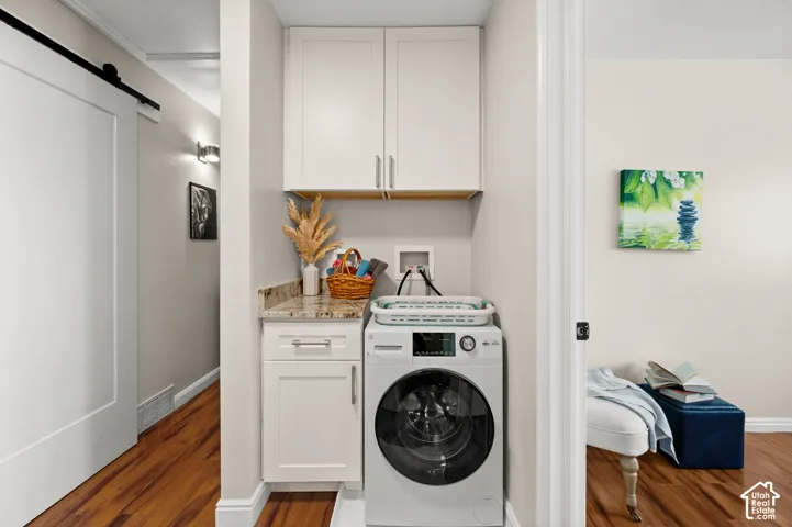 Dedicated laundry area featuring a front-load washing machine, white cabinetry, a built-in counter with a stone surface, and wood-finish flooring