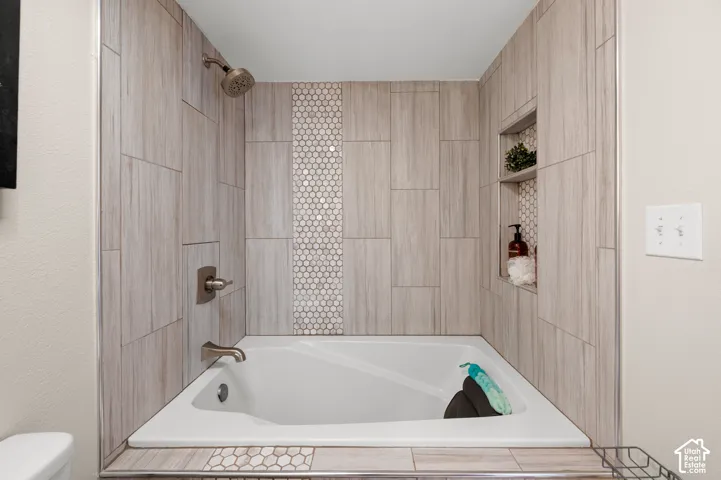 Alcove bathtub featuring a tiled surround, accent mosaic tile, and built-in shower niches
