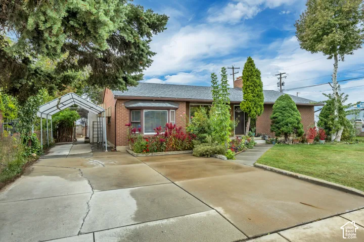 Brick exterior with a gray shingle roof, bay window, concrete driveway, and front lawn