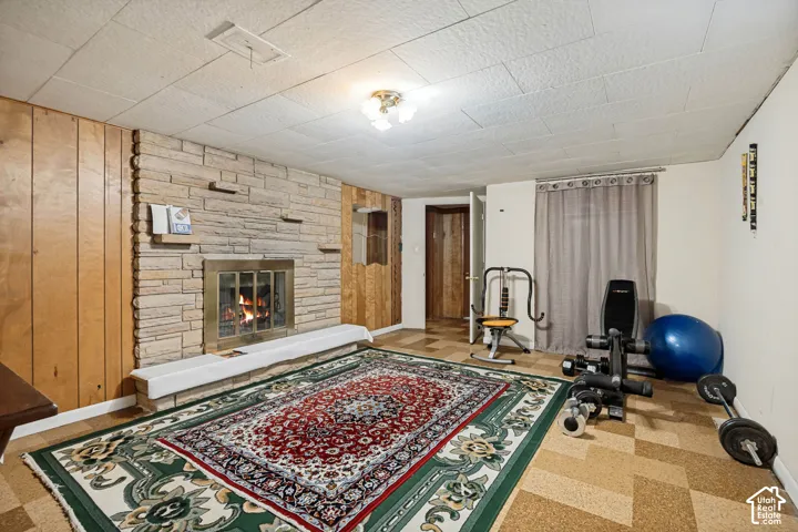 Stone-clad fireplace with a brass-trimmed insert, wood-paneled wall, textured ceiling tiles, and patterned flooring