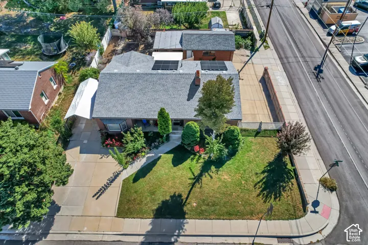 Pitched roof residence with solar panels, an established front yard, an extended driveway, and a paved side yard