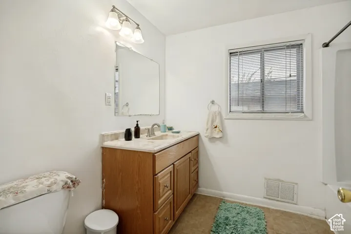 Bathroom featuring a wood-finish vanity with a single sink, an integrated countertop, and a wall-mounted mirror