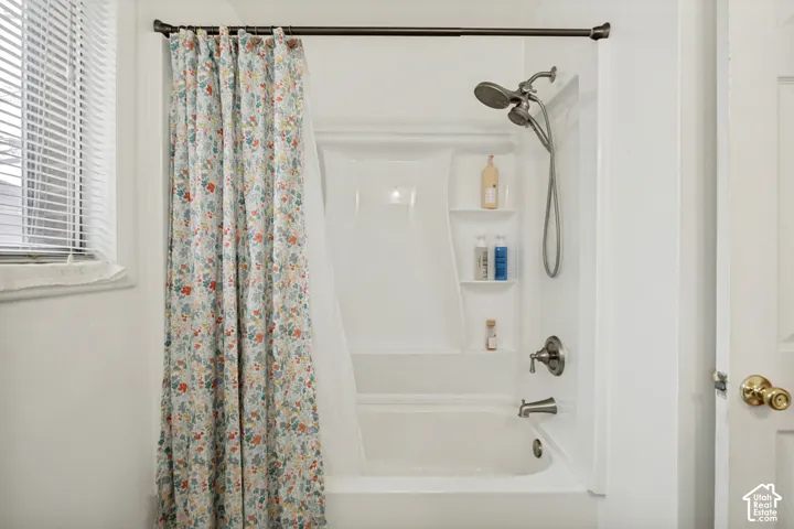 White tub and shower combination with an integrated multi-shelf caddy, a handheld shower fixture, and brushed nickel hardware