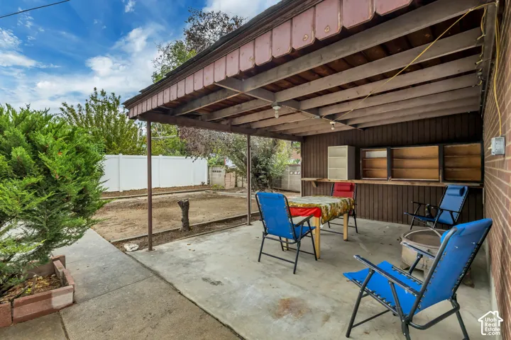 Covered concrete patio with exposed wood beam ceiling, brick exterior wall, and built-in wood-finish shelving