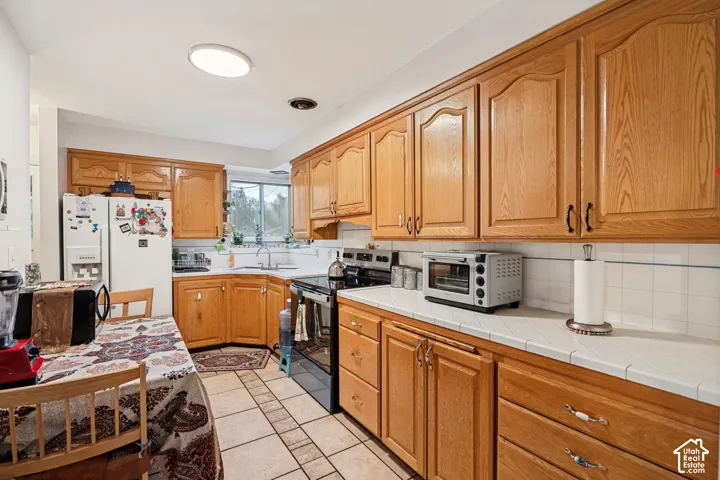 Kitchen featuring wood-finish cabinetry, tile countertops, white subway tile backsplash, and tile flooring