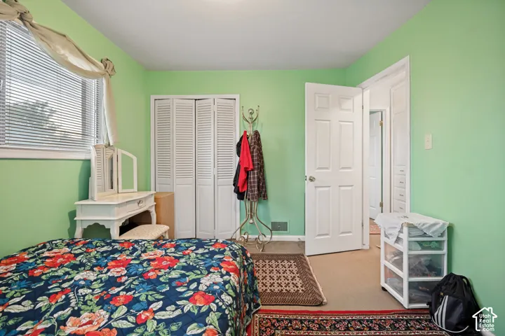 Bright secondary bedroom with soft green walls, large closet with louvered doors, wood-finish flooring, and multiple windows providing natural light