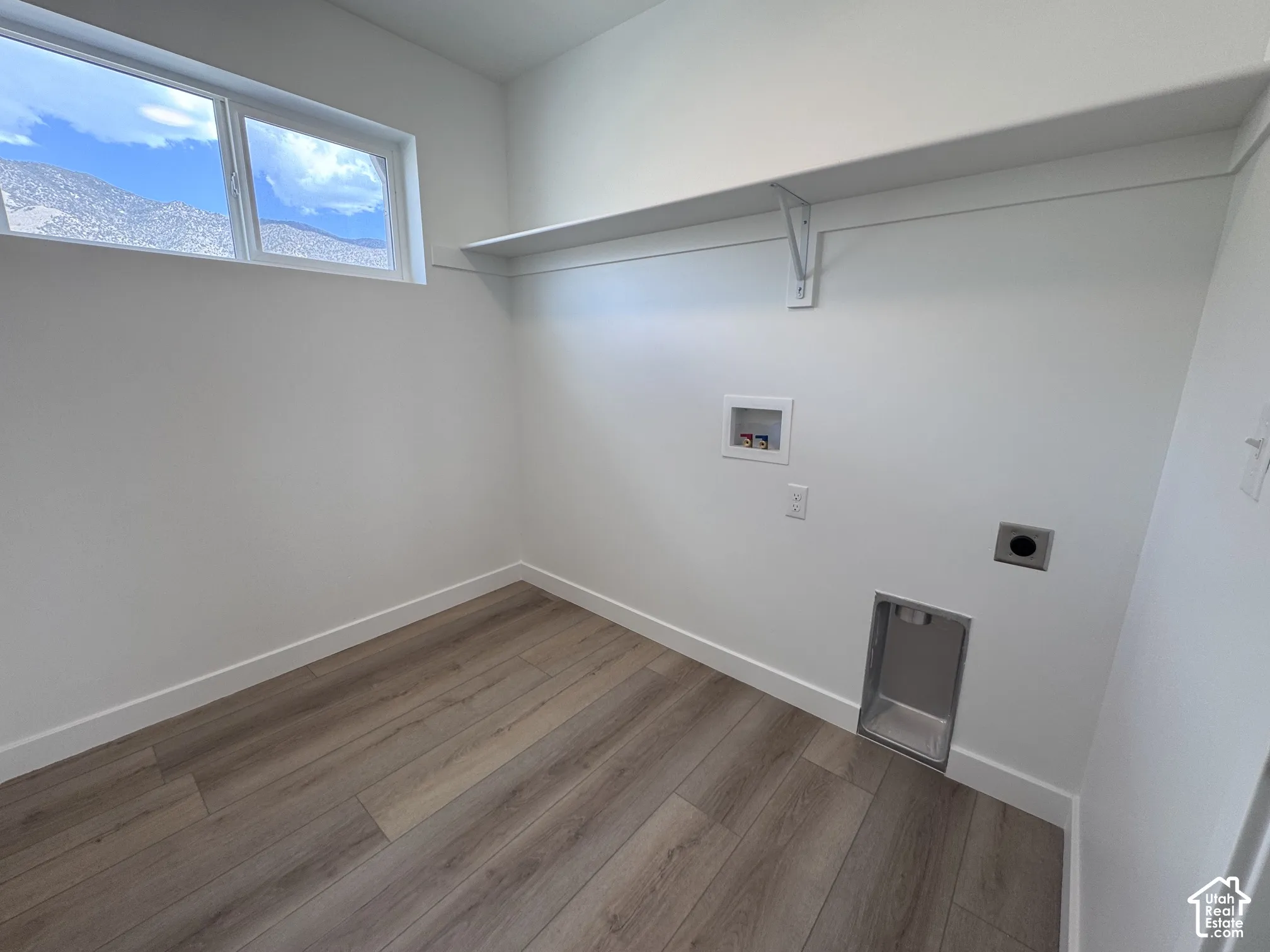 Dedicated laundry space with wood-finish flooring, a wall-mounted shelf, and a horizontal window