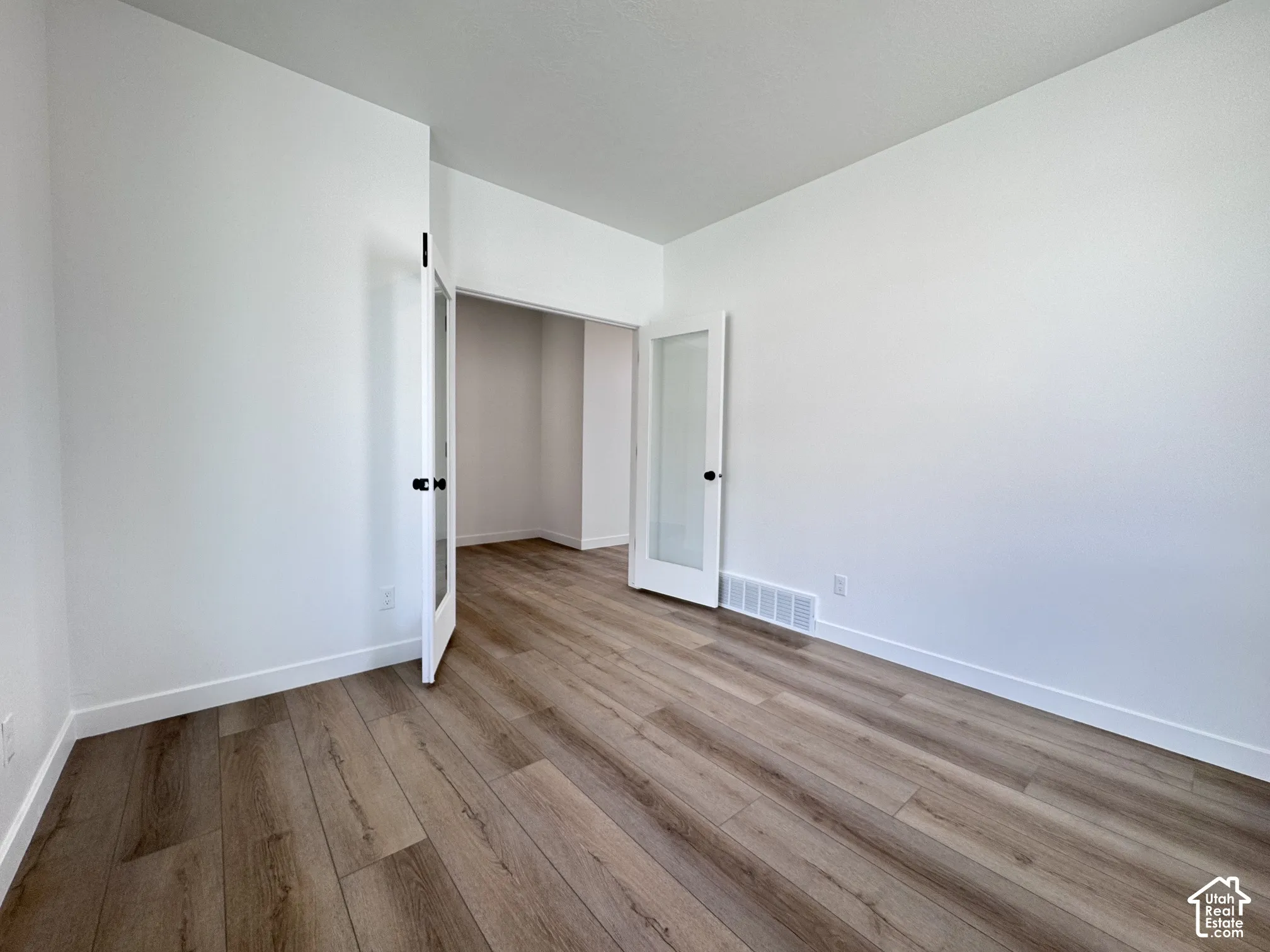 Wood-finish flooring, white walls, and French doors with frosted glass panels